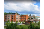 Exterior view of a multi-story senior living facility named The Community at Rockhill, featuring a brick facade, balconies, and a covered entrance with greenery and a partly cloudy sky in the background.