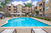 Outdoor pool area with lounge chairs and beige apartment buildings.