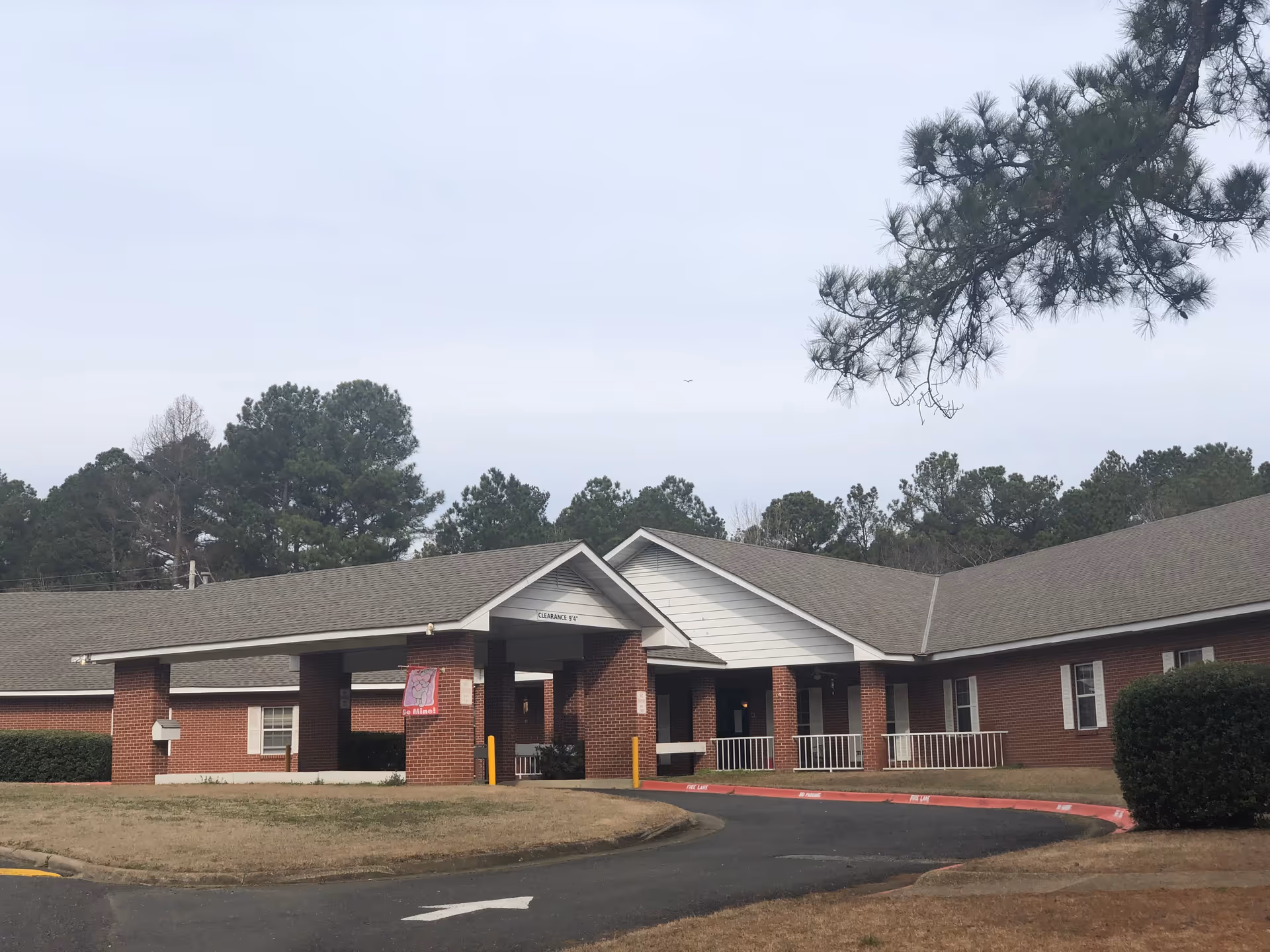 Brick senior living facility entrance with curved driveway and surrounding trees.