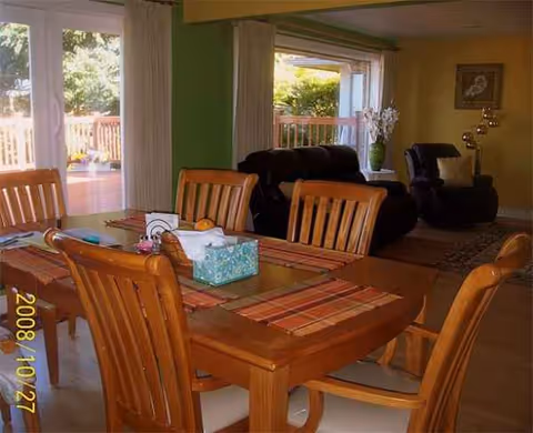 Wood dining table and chairs in a bright communal room with recliners nearby.