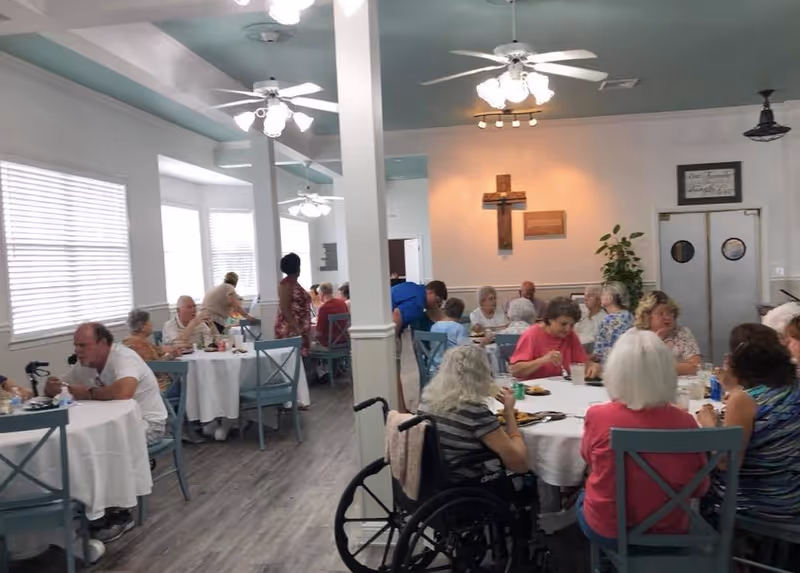 A dining room in a senior living facility with residents seated at tables eating and socializing.