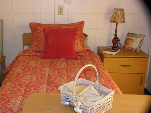A bedroom with a red-patterned bedspread, pillows, nightstand, and a basket.