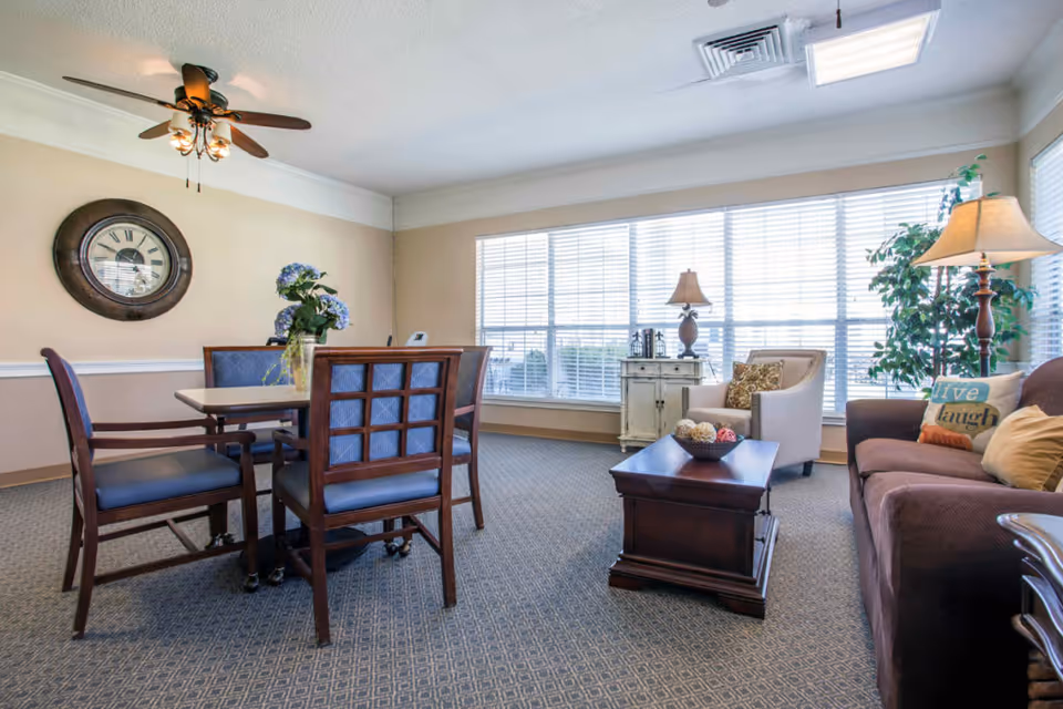 Bright communal living room with a dining table and chairs, a sofa and armchair, coffee table and large windows.