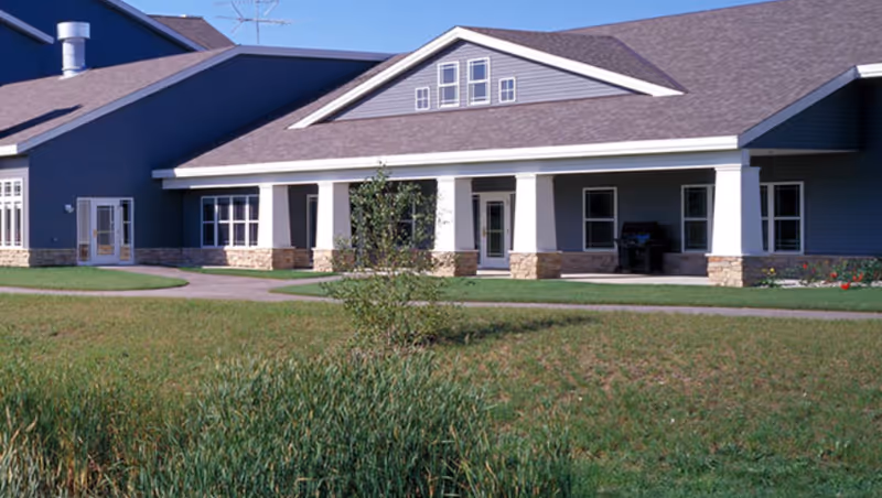 Front exterior of a single-story building with a covered porch, columns, and a grassy lawn.