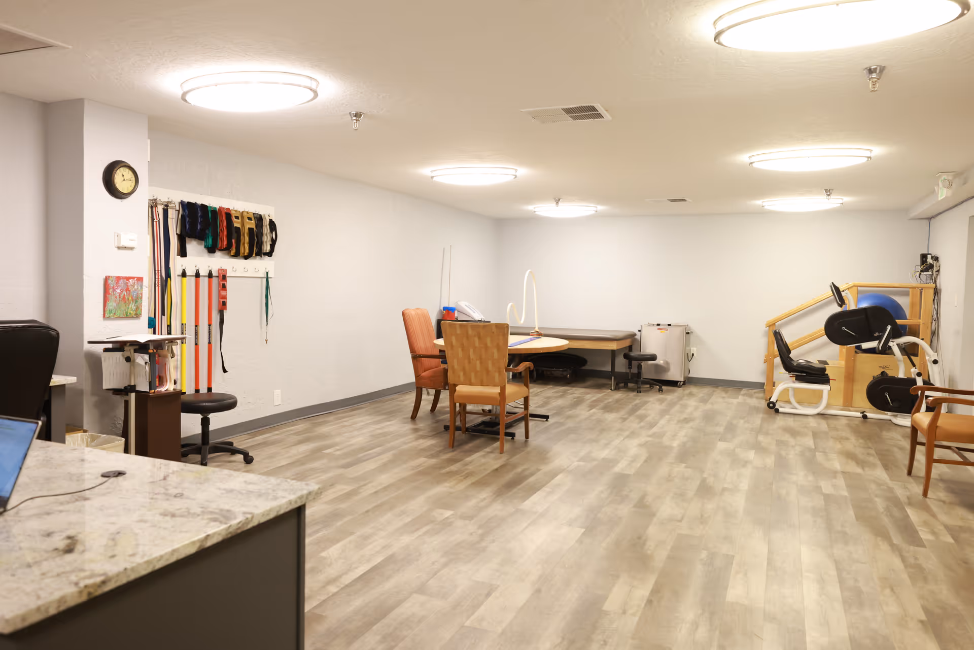 Spacious multipurpose therapy room with tables, chairs, exercise equipment and resistance bands on the wall.