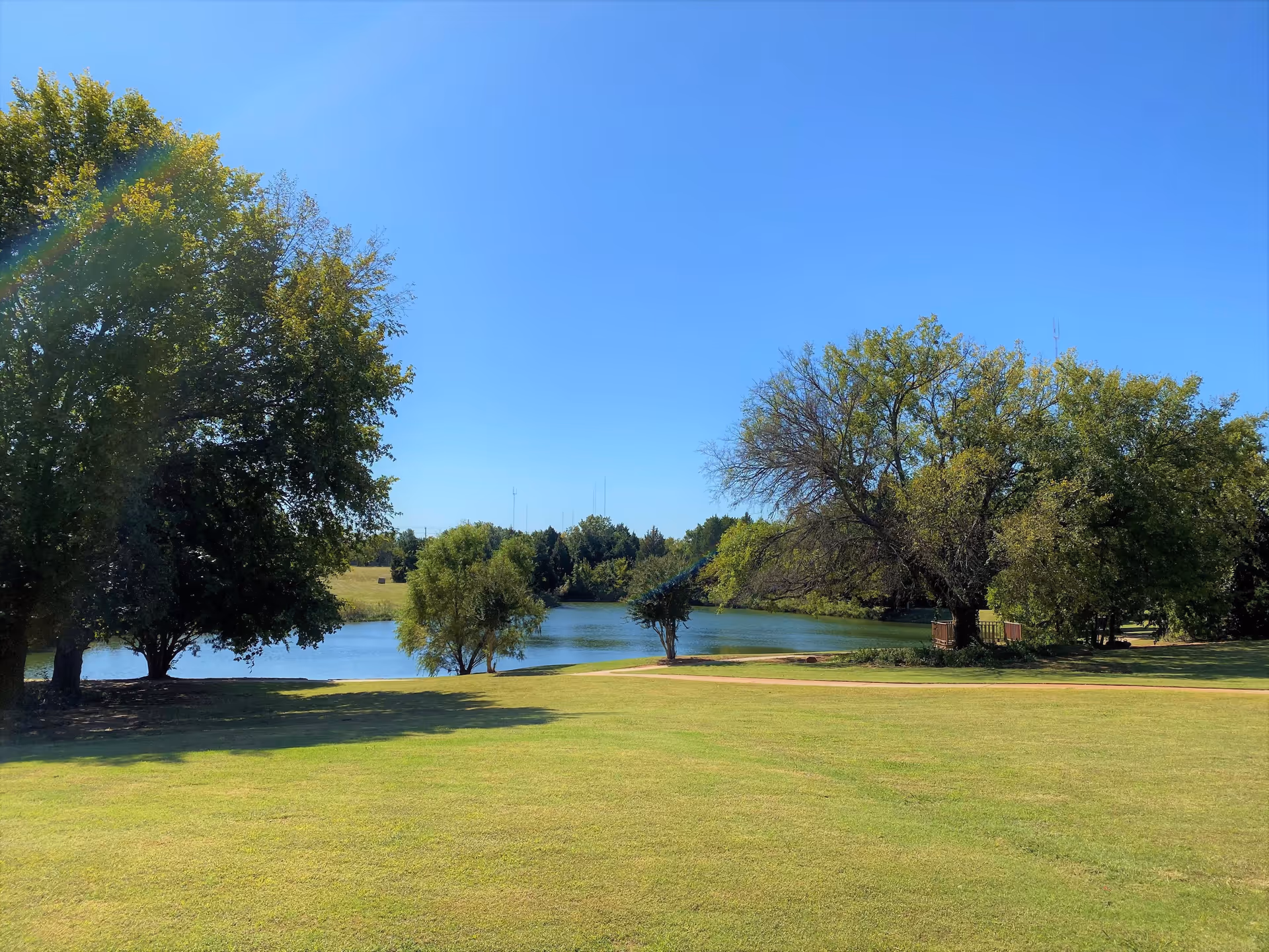 A scenic outdoor view of a grassy lawn with several trees surrounding a small pond under a clear blue sky at Tealridge Retirement Community.
