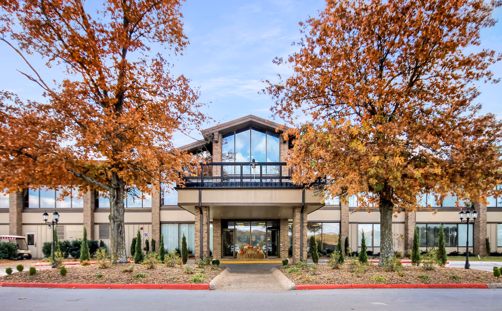 Two autumn trees frame a modern senior living facility entrance with glass doors.
