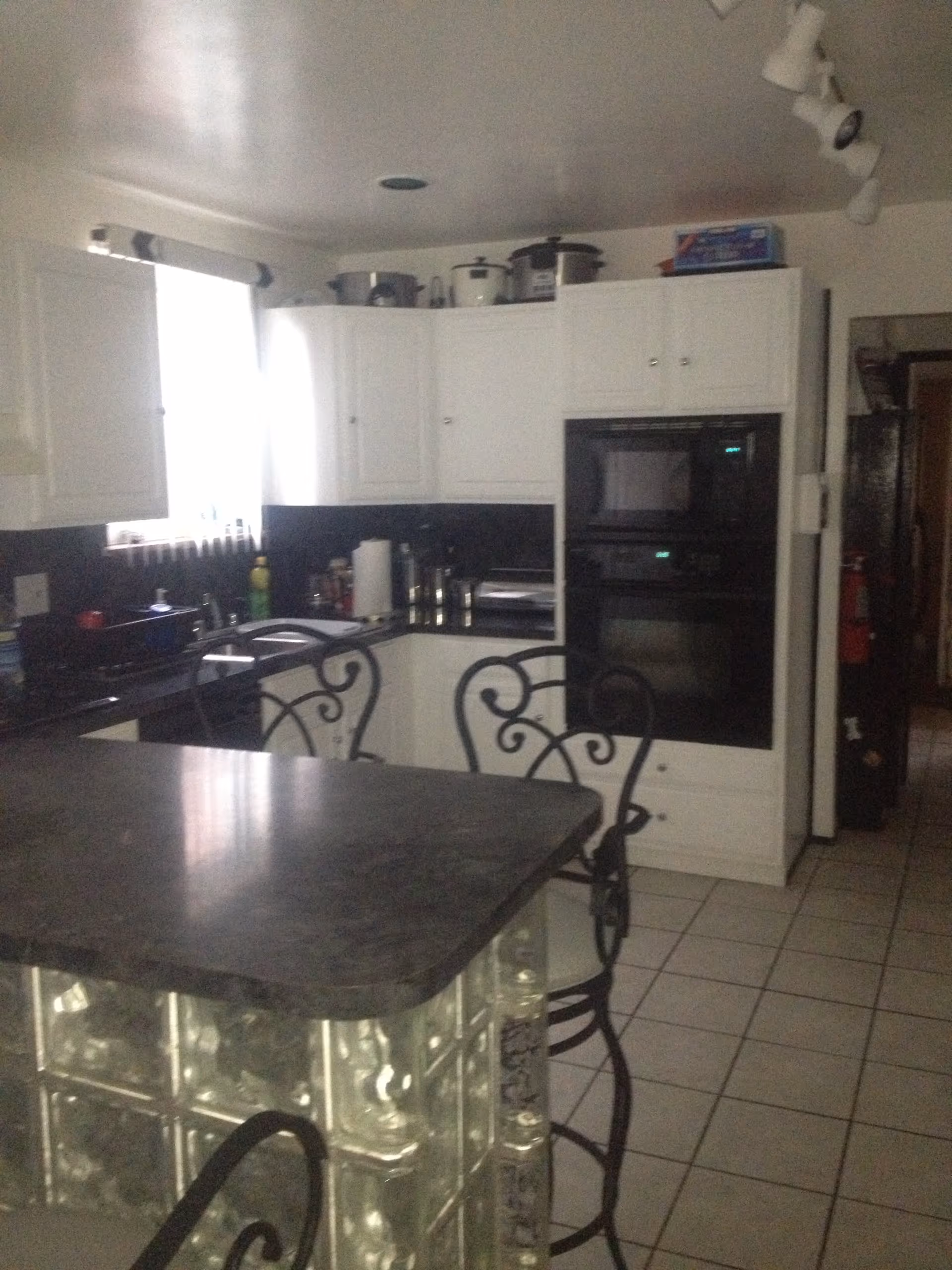 Kitchen with white cabinets, black countertops, a glass-block base island and wrought-iron bar stools.