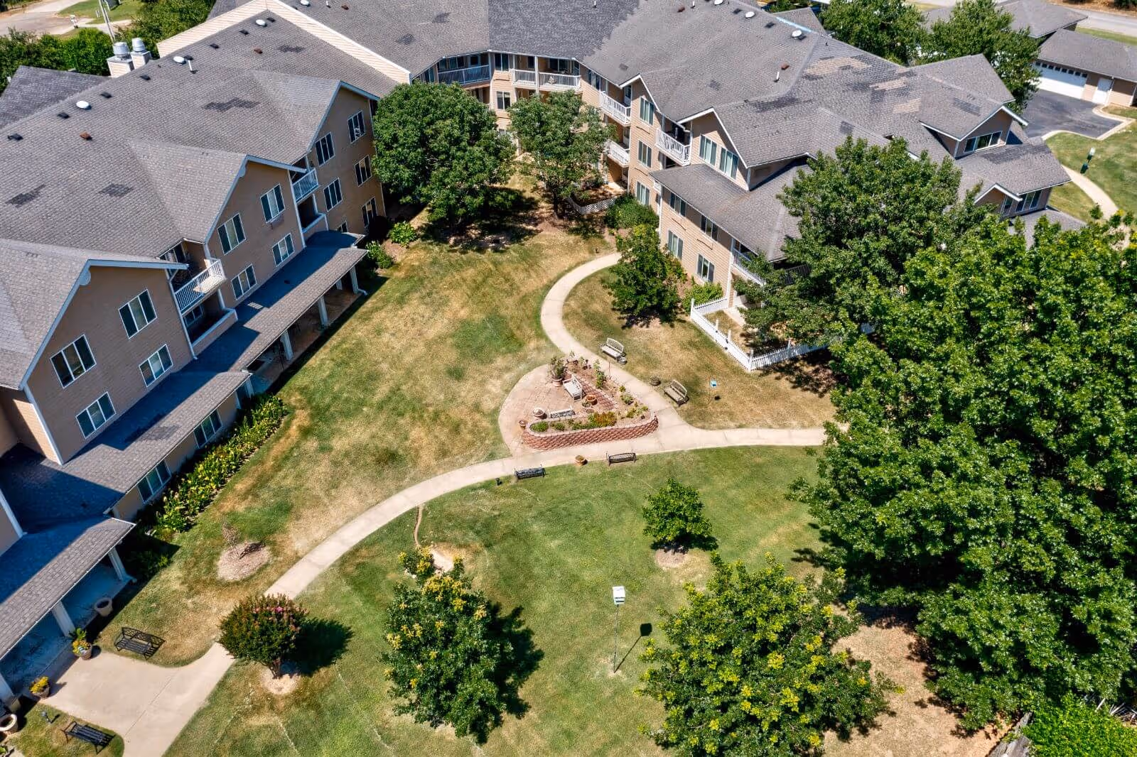 Aerial view of a U-shaped residential building surrounding a landscaped courtyard with walking paths, benches, and trees.
