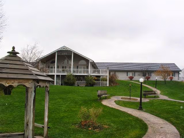 Green lawn with a winding path, benches and a gazebo leading up to the front of a two-story senior living building with balconies.