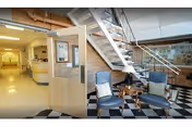 Bright lobby area with checkered floor, seating, and a staircase against a brick wall.