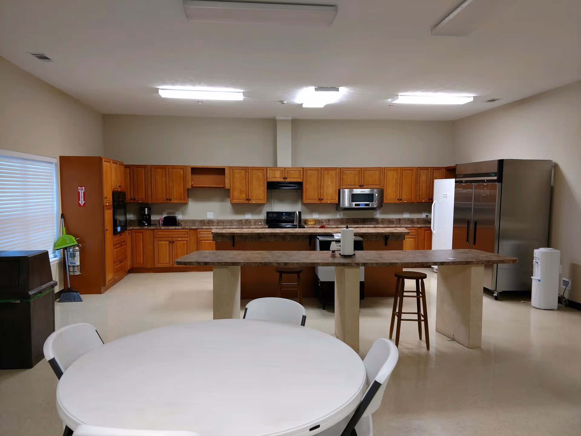 Large communal kitchen with a long island, wooden cabinets, stainless appliances, and a round table with chairs in the foreground.