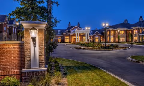 Evening exterior view of Waltonwood Providence with illuminated entrance and circular driveway.