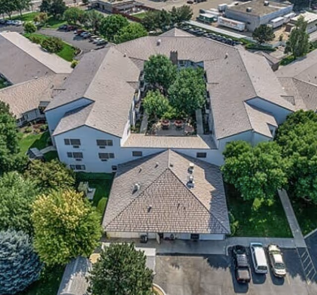 Aerial view of a multi-wing senior living building arranged around a tree-filled central courtyard with a parking lot in front.