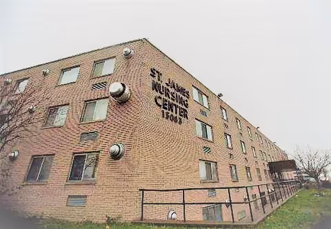 Brick exterior of St. James Nursing & Physical Rehabilitation Center showing multiple windows, circular vents, and a ground-level railing.