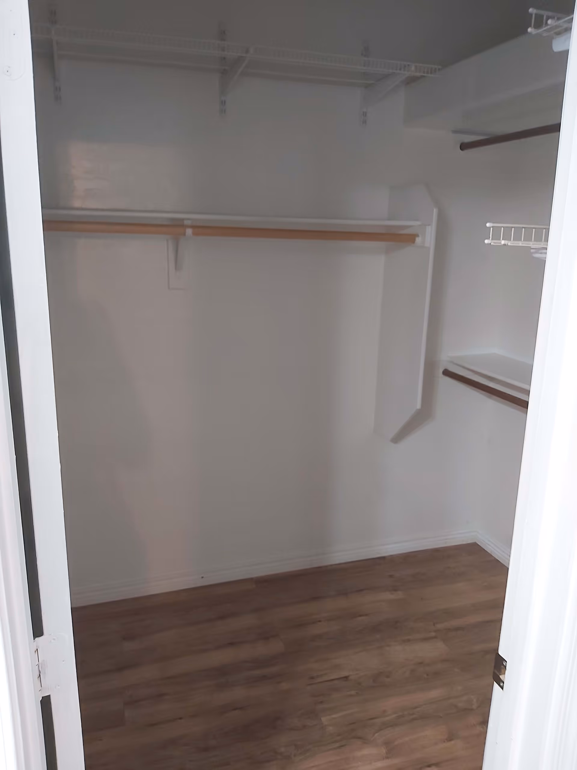 Empty walk-in closet with wooden floor, white walls, and multiple shelves and hanging rods for storage.