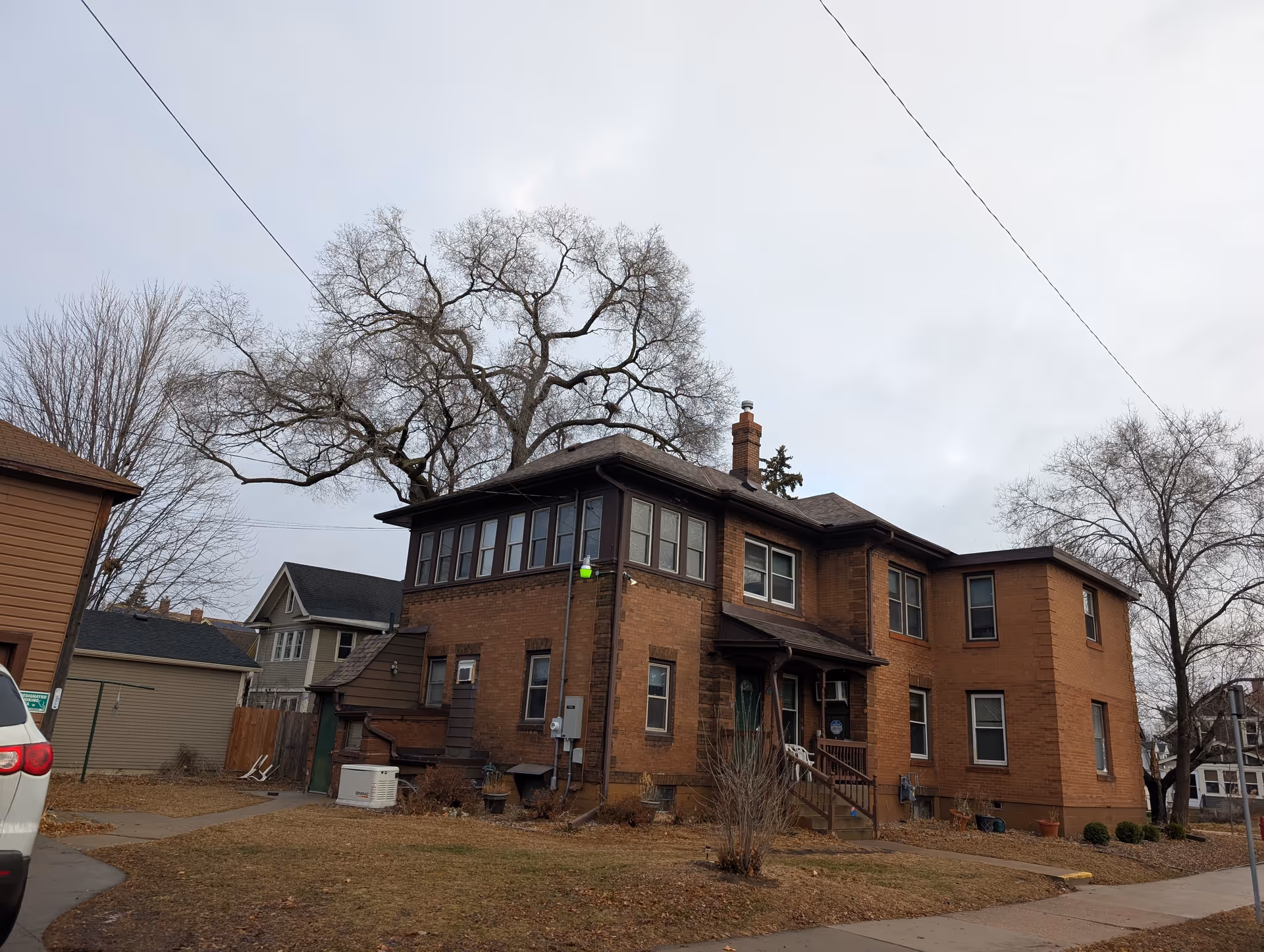 Exterior view of a two-story brick building with multiple windows and a small porch entrance, surrounded by leafless trees and a lawn with dry grass under an overcast sky.