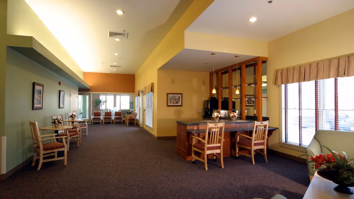 Spacious communal lounge with seating, small tables, a counter with chairs, and large windows letting in light.