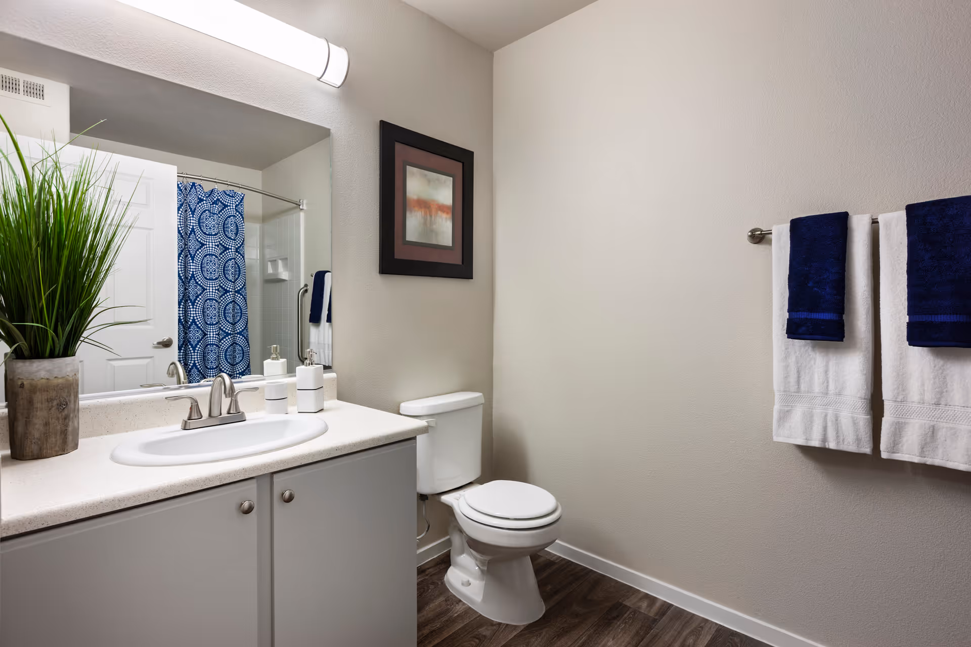 Bathroom with a sink vanity and mirror, toilet, blue-patterned shower curtain, and neatly hung towels.