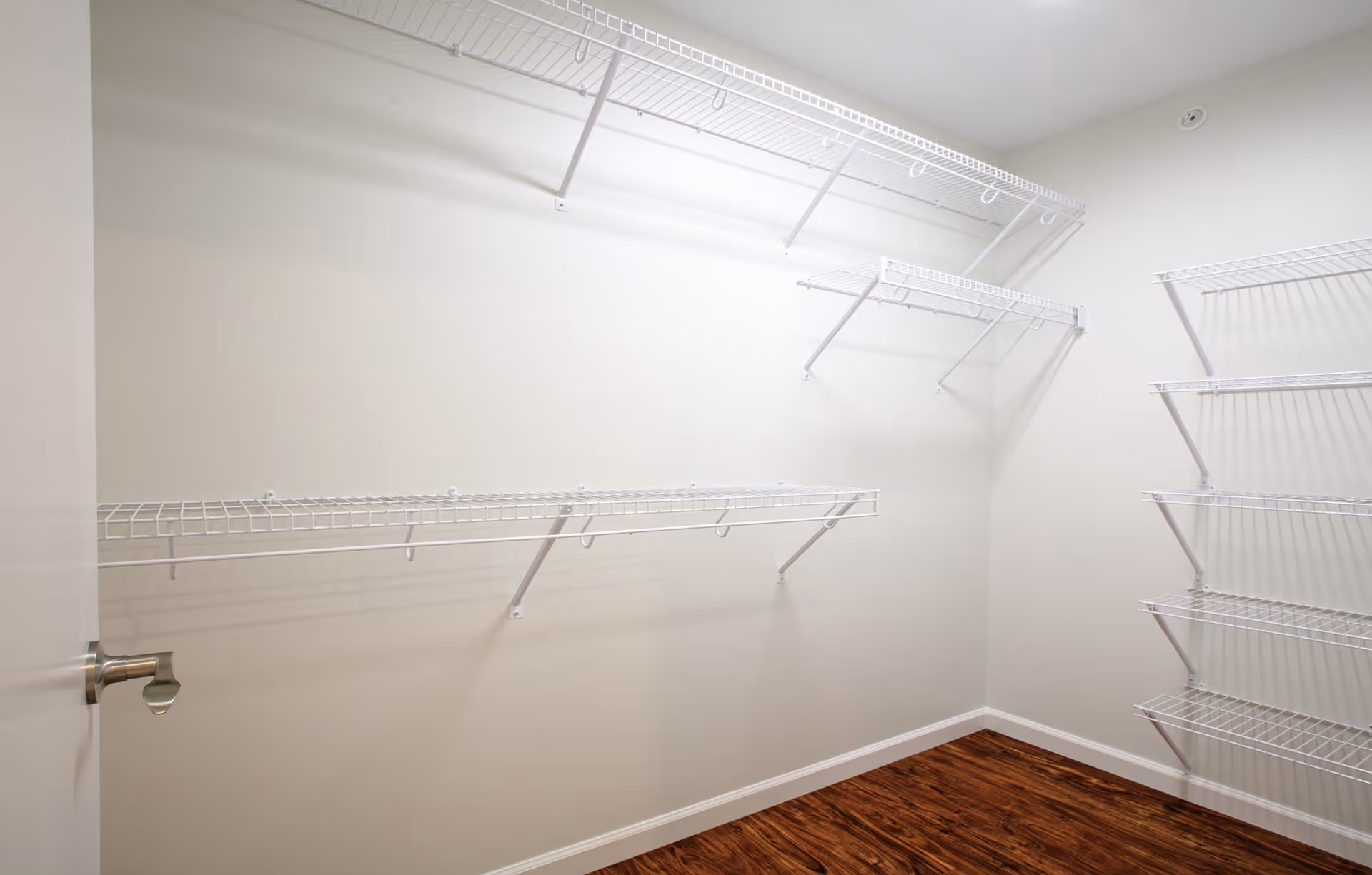 Empty walk-in closet with white wire shelving on three walls and wood flooring.