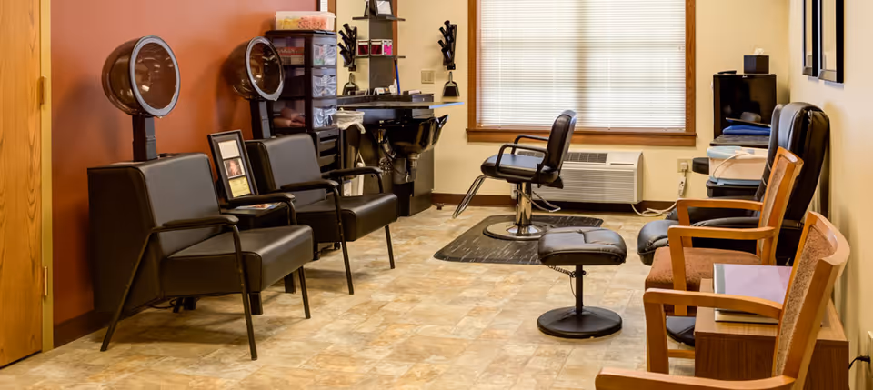Salon-style room with styling chairs, hooded hair dryers, a shampoo sink and waiting chairs.