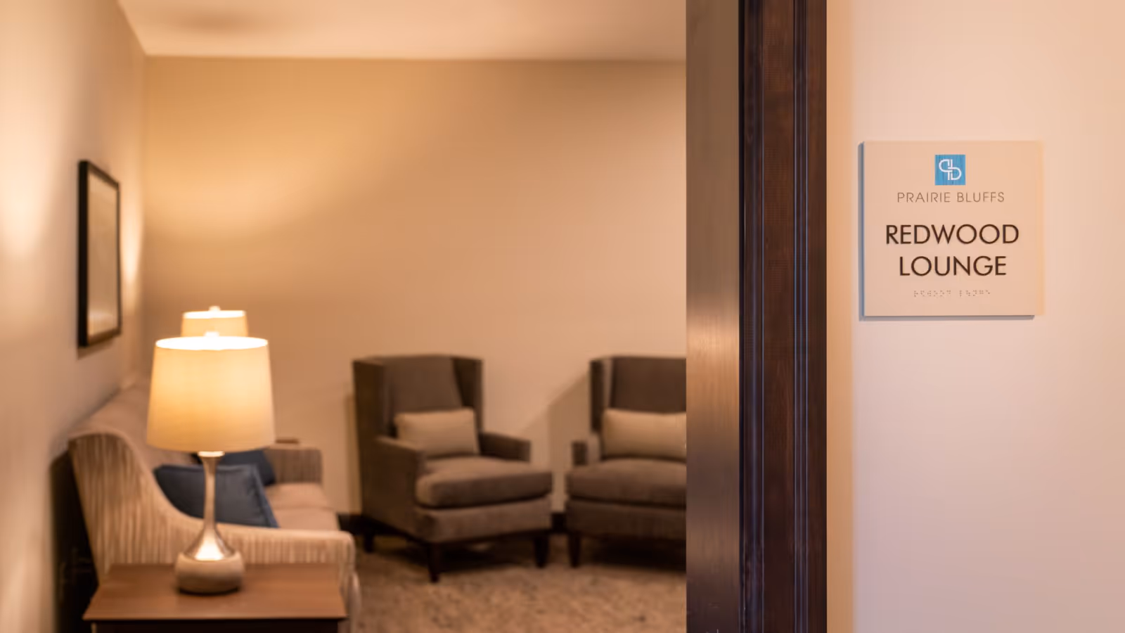 Entrance to the Redwood Lounge showing a cozy seating area with armchairs, a sofa, and a table lamp.