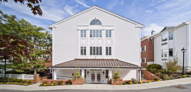 White, multi-story nursing facility facade with central arched window and covered entrance.