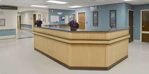 A curved wooden reception desk with purple flowers in a blue-walled hallway.