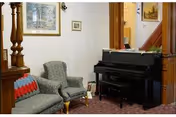 Small sitting area with two upholstered armchairs, a black upright piano, and framed artwork on the wall.
