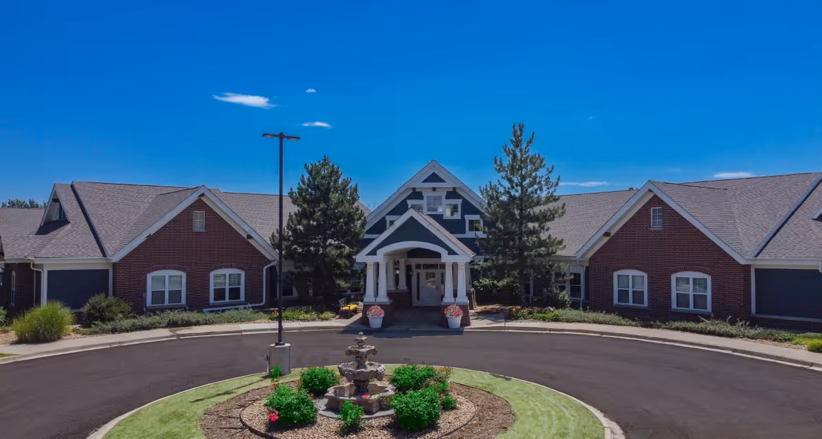 Front exterior view of Balfour Cherrywood facility with a circular driveway, landscaped garden with a fountain in the center, and a clear blue sky above.