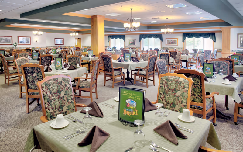 Large dining room with many set tables, floral-upholstered chairs, and place settings.
