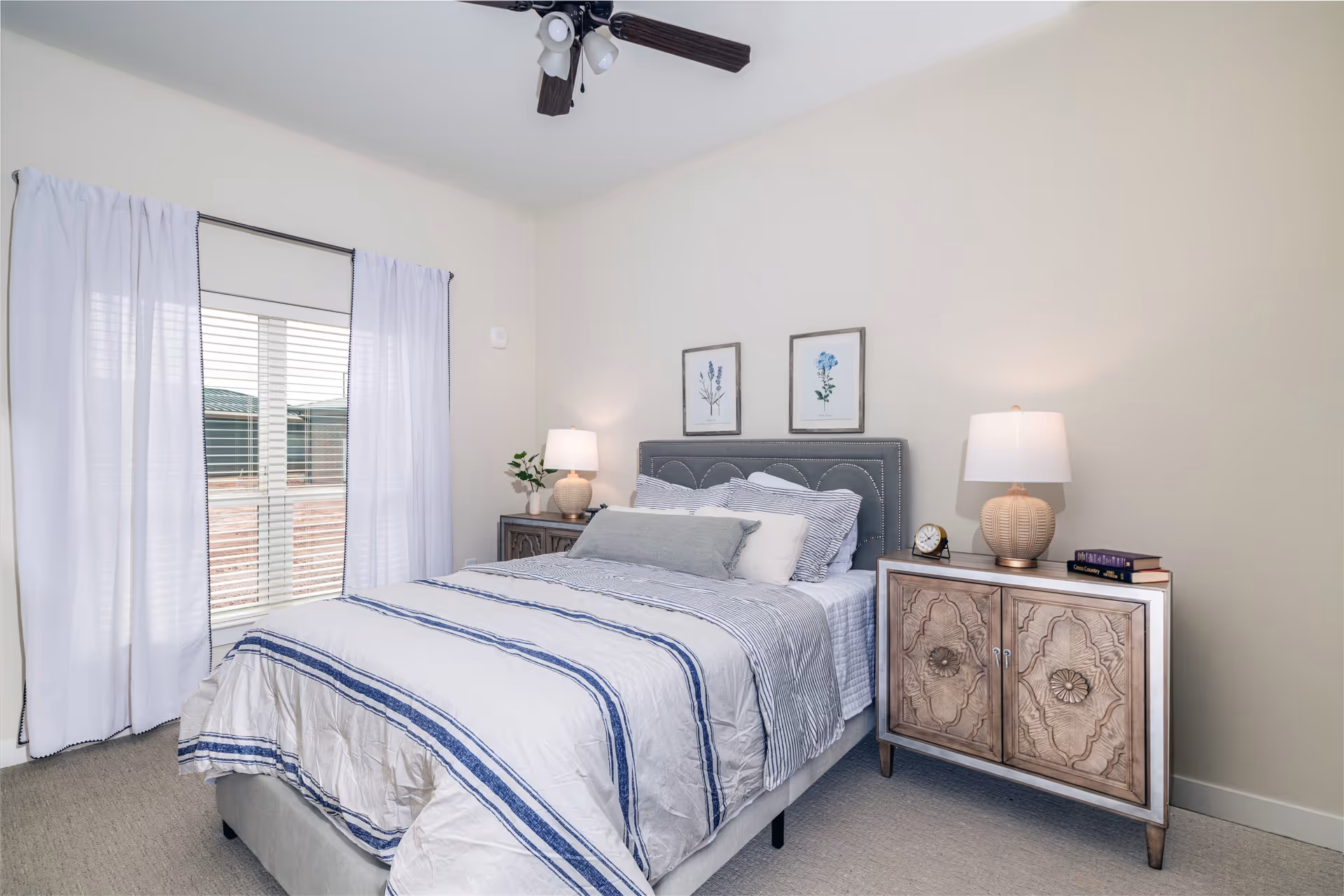 A neatly made bedroom with a bed, two nightstands, lamps, and framed artwork.