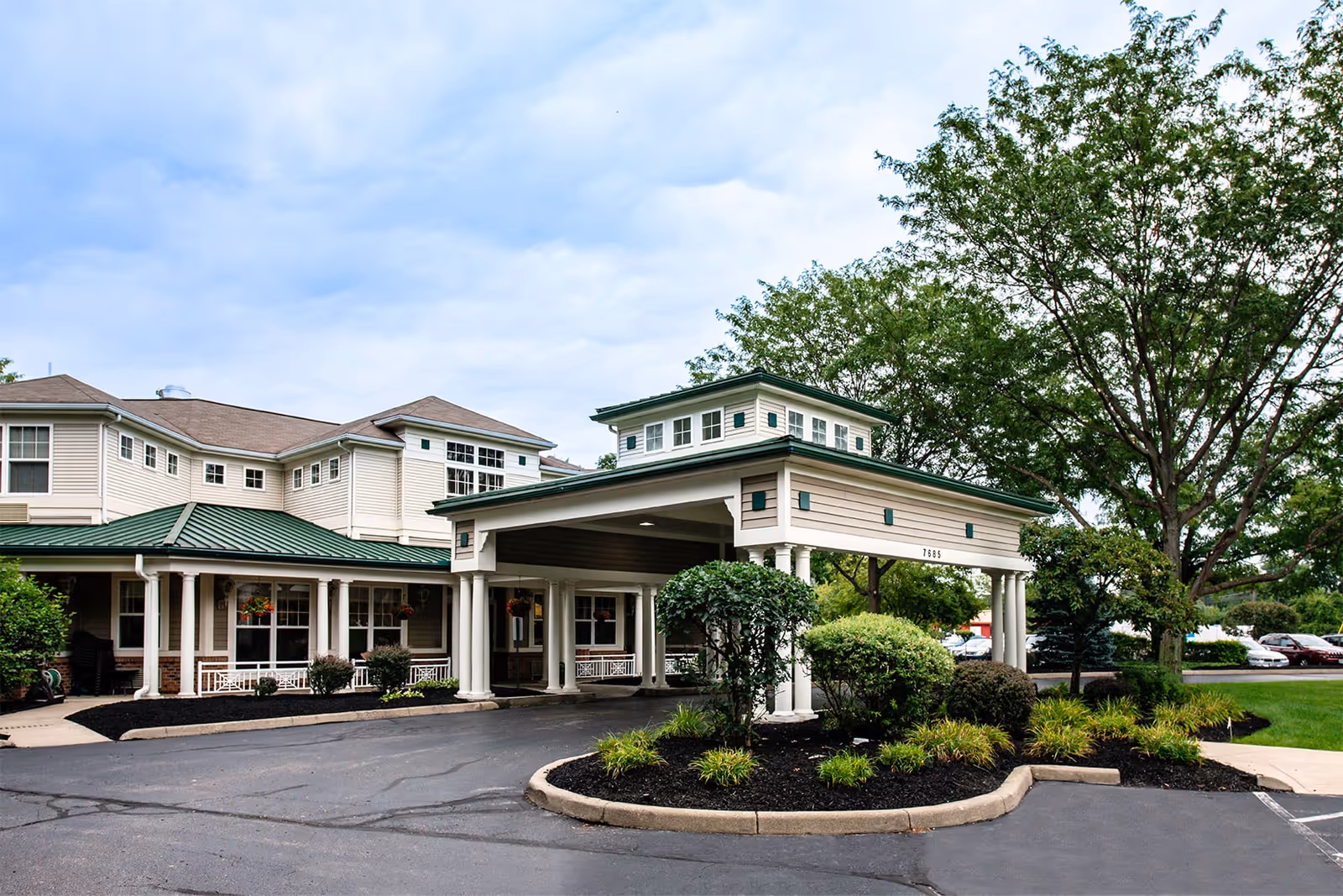 Front entrance of a senior living building featuring a covered porte-cochère with white columns and landscaped driveway.