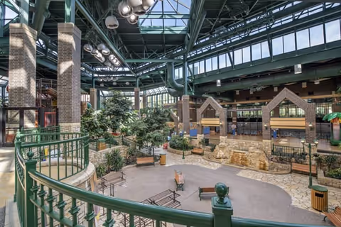 Large indoor atrium with a glass skylight, greenery, benches, and a stone water feature.