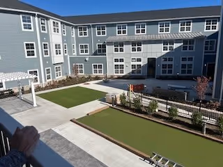 Enclosed sunny courtyard of a multi-story senior living building featuring bocce/putting greens, paved walkways, seating areas and balconies.