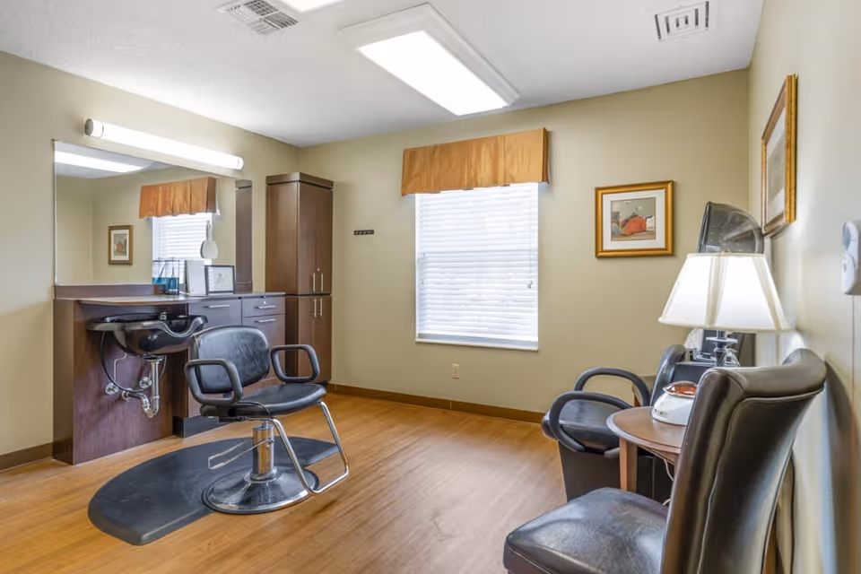Small salon room with a styling chair, wash sink, cabinetry, and additional seating beside a window.