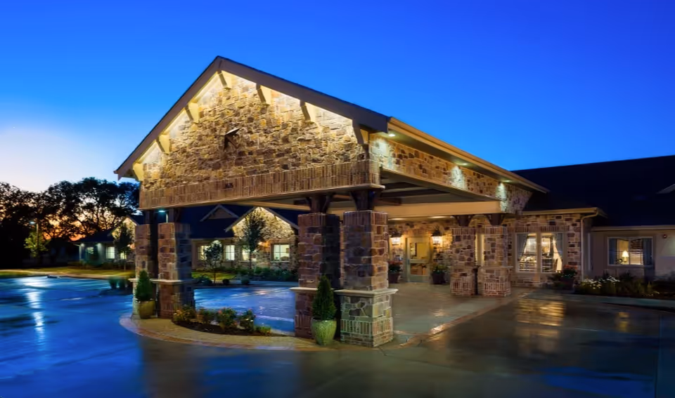 Stone-clad senior living facility entrance with a covered porte-cochère at dusk.