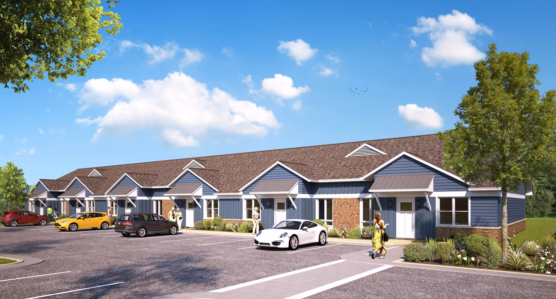Single-story row of blue townhome-style senior living units with parking, cars, landscaping and a few people under a blue sky.