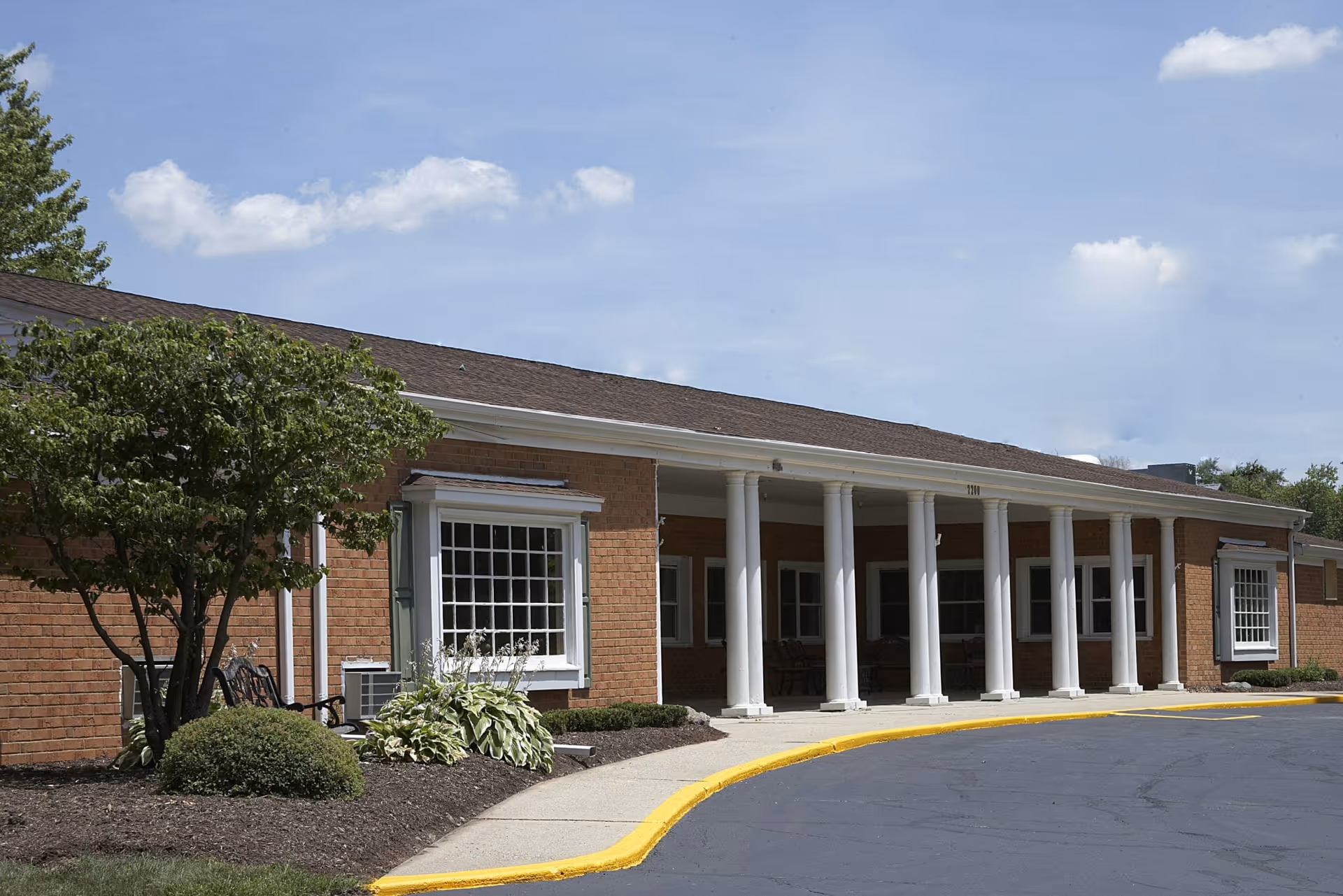 Front entrance of a single-story brick building with white columns, a curved driveway, and landscaping.