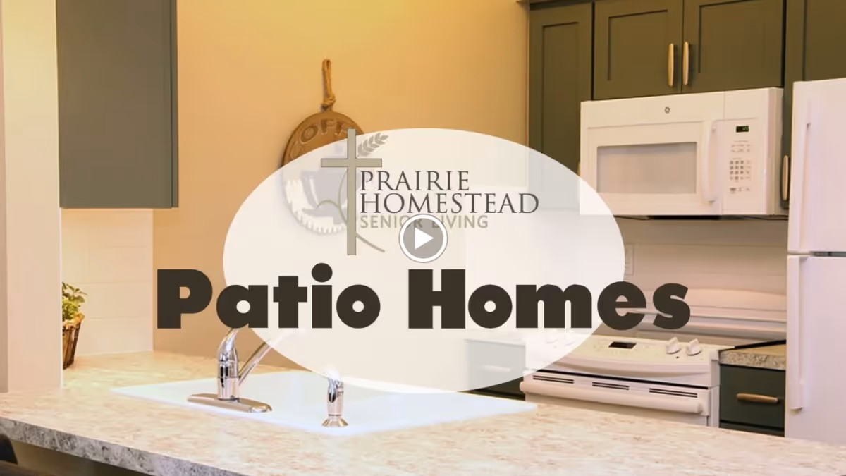 Kitchen with a sink and countertop facing a stove, microwave, refrigerator and cabinets with an overlaid 'Prairie Homestead Senior Living Patio Homes' graphic.