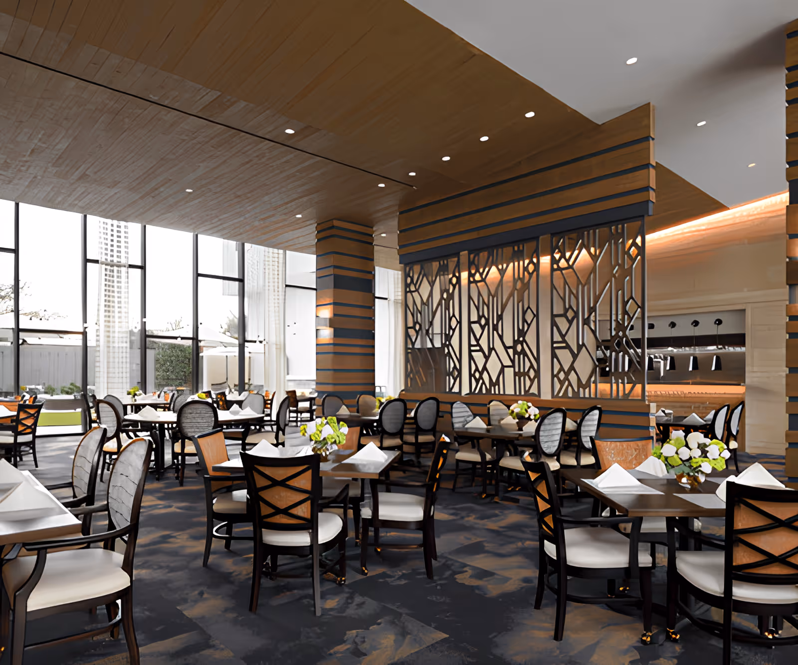 Spacious modern dining room with multiple set tables and chairs, decorative partition, large windows, and floral centerpieces.