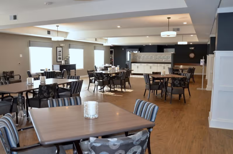 Spacious communal dining room with multiple wooden tables and chairs, pendant lights, and a service counter in the back.