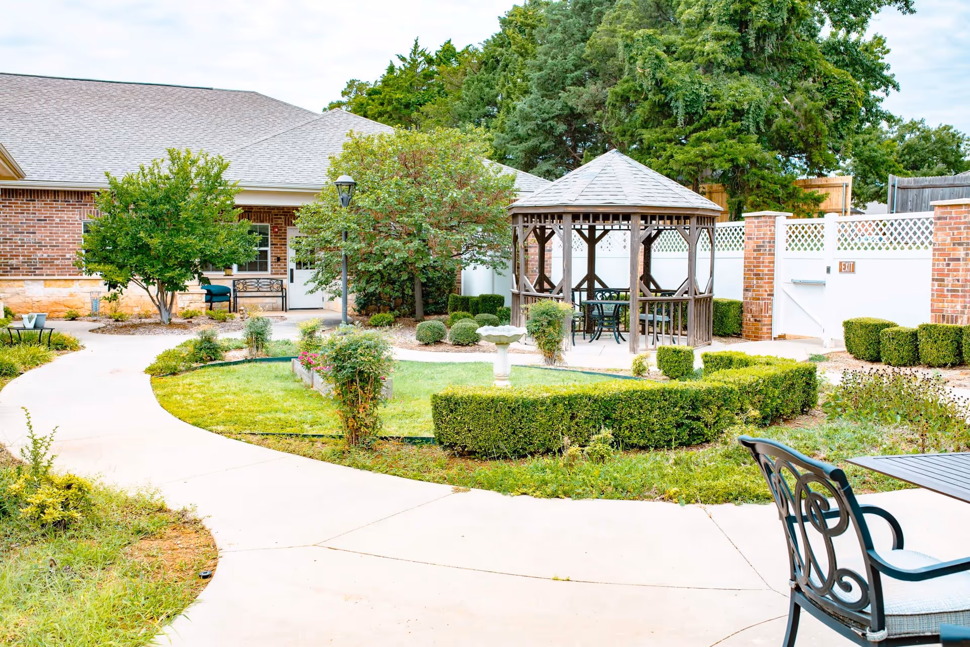 Courtyard with a wooden gazebo, paved walkways, trimmed hedges, outdoor seating, and the brick exterior of a building.