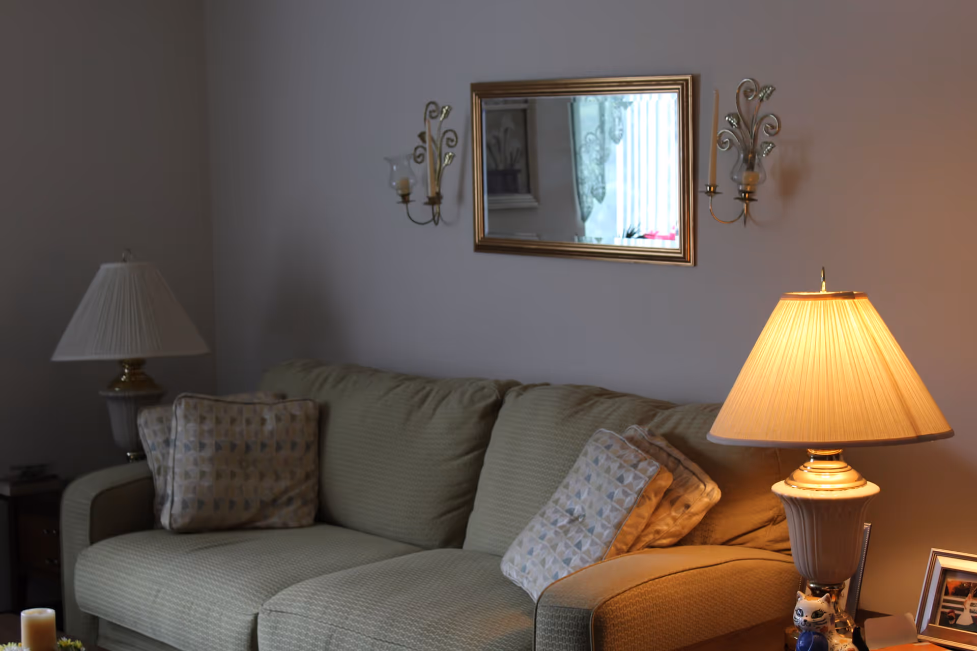 A living room with a green sofa, patterned throw pillows, a mirror on the wall, and two table lamps.