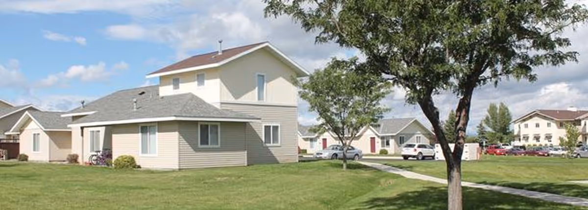 Exterior view of a senior apartments complex with green lawns, trees, and parked cars.