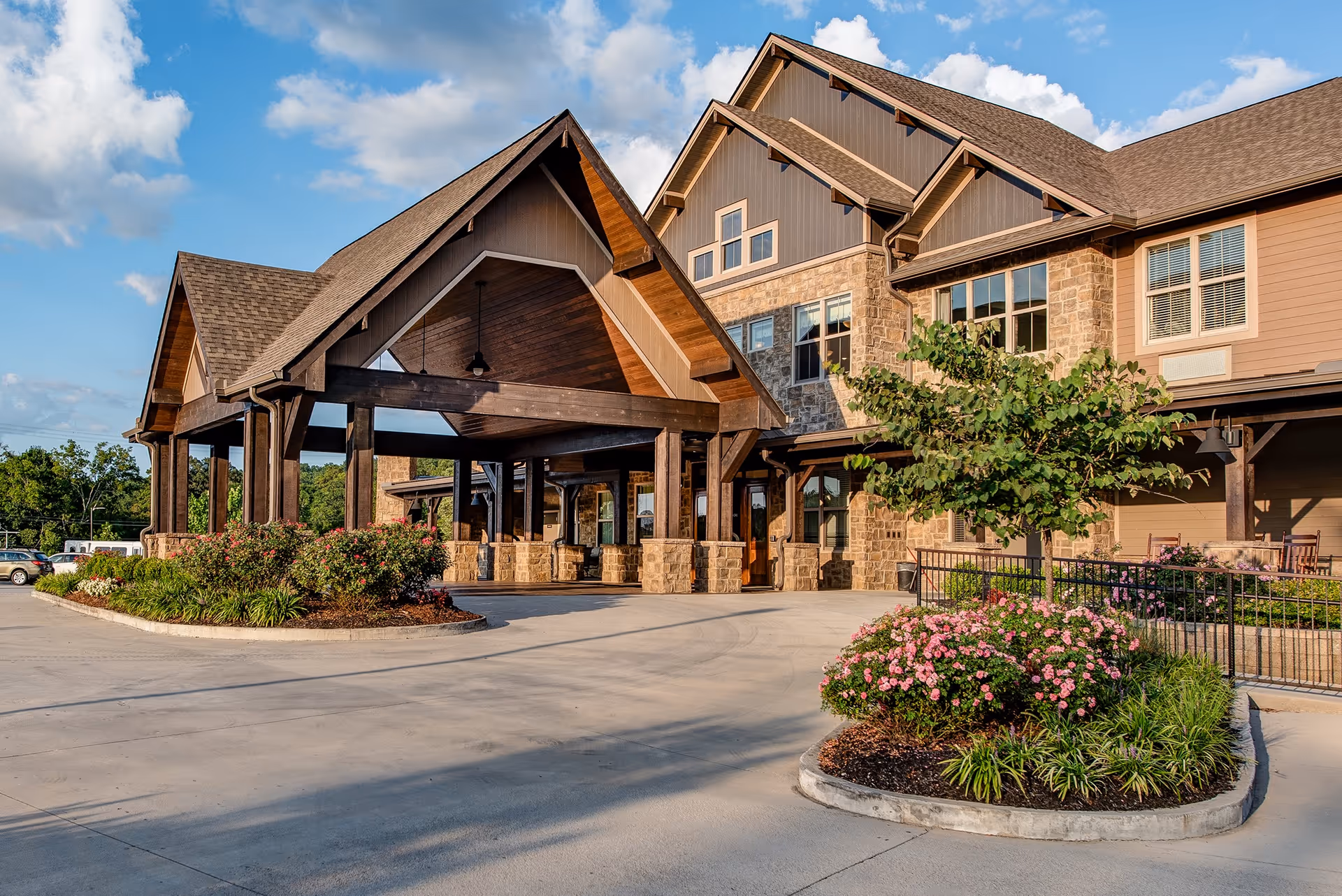 Front entrance of a multi-story stone and wood senior living building with a covered porte-cochere and landscaped flowerbeds.