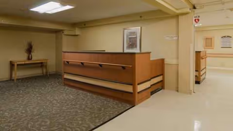 Reception desk and hallway in a quiet senior living facility lobby with carpeted floor.