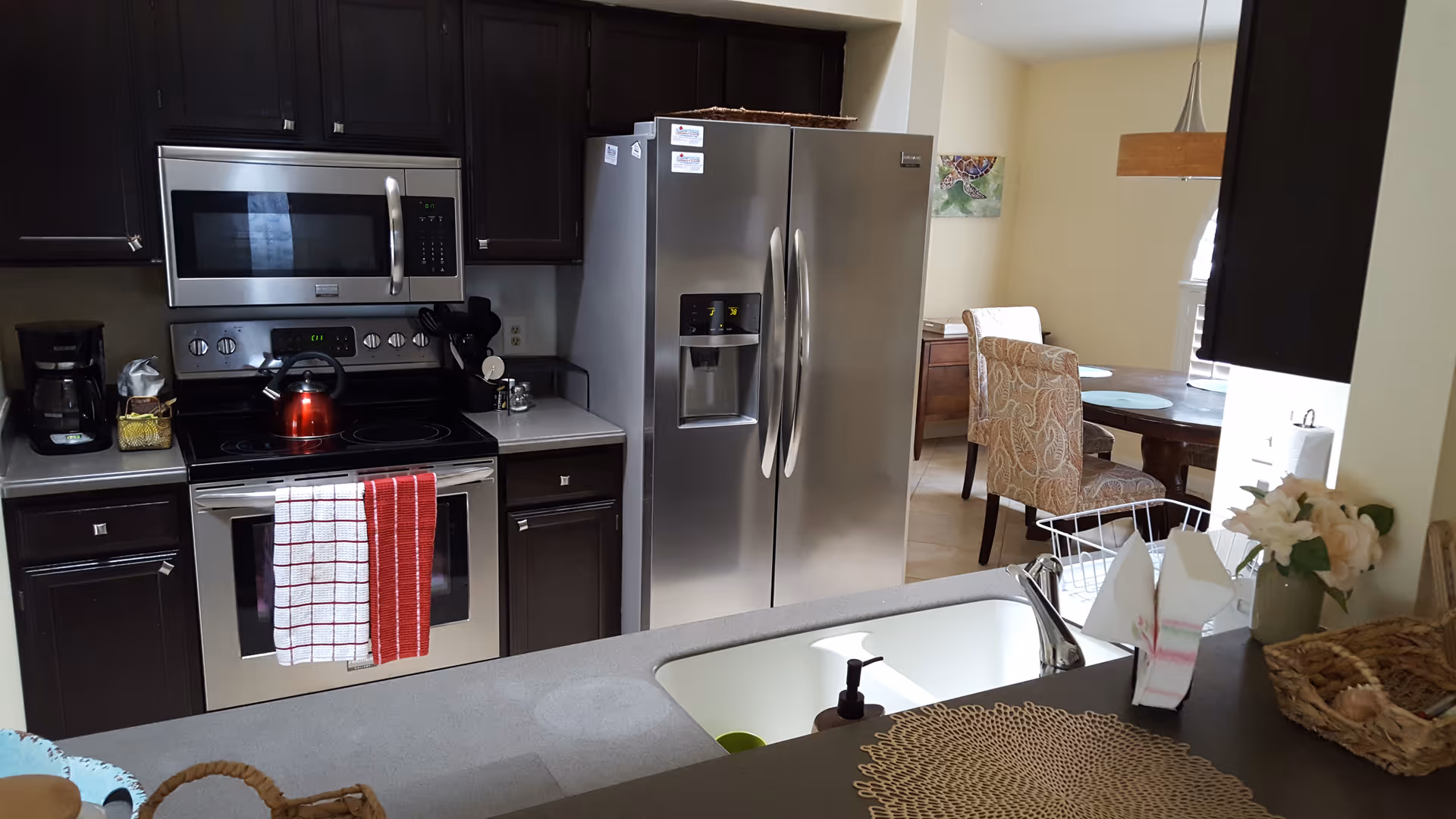 Open kitchen featuring stainless steel refrigerator and oven, a sink in the foreground, and a small dining area beyond.