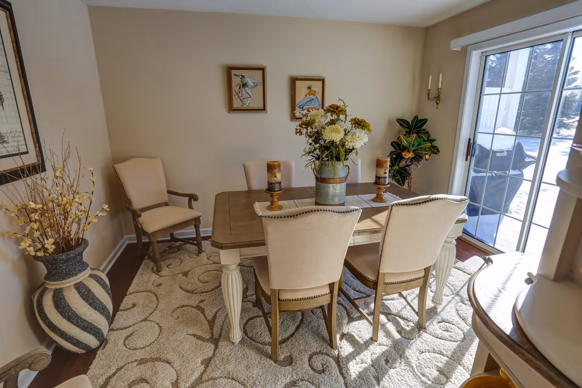 Bright dining room with a wooden table, upholstered chairs, a floral centerpiece, and a sliding glass door to the outside.