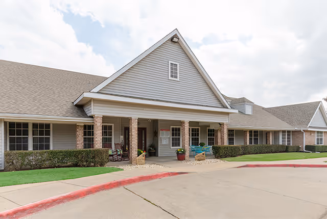 Exterior view of Cleburne Court senior living facility with a covered entrance and seating.